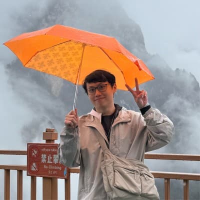 Ryan Tan holding an orange umbrella in the mountains
